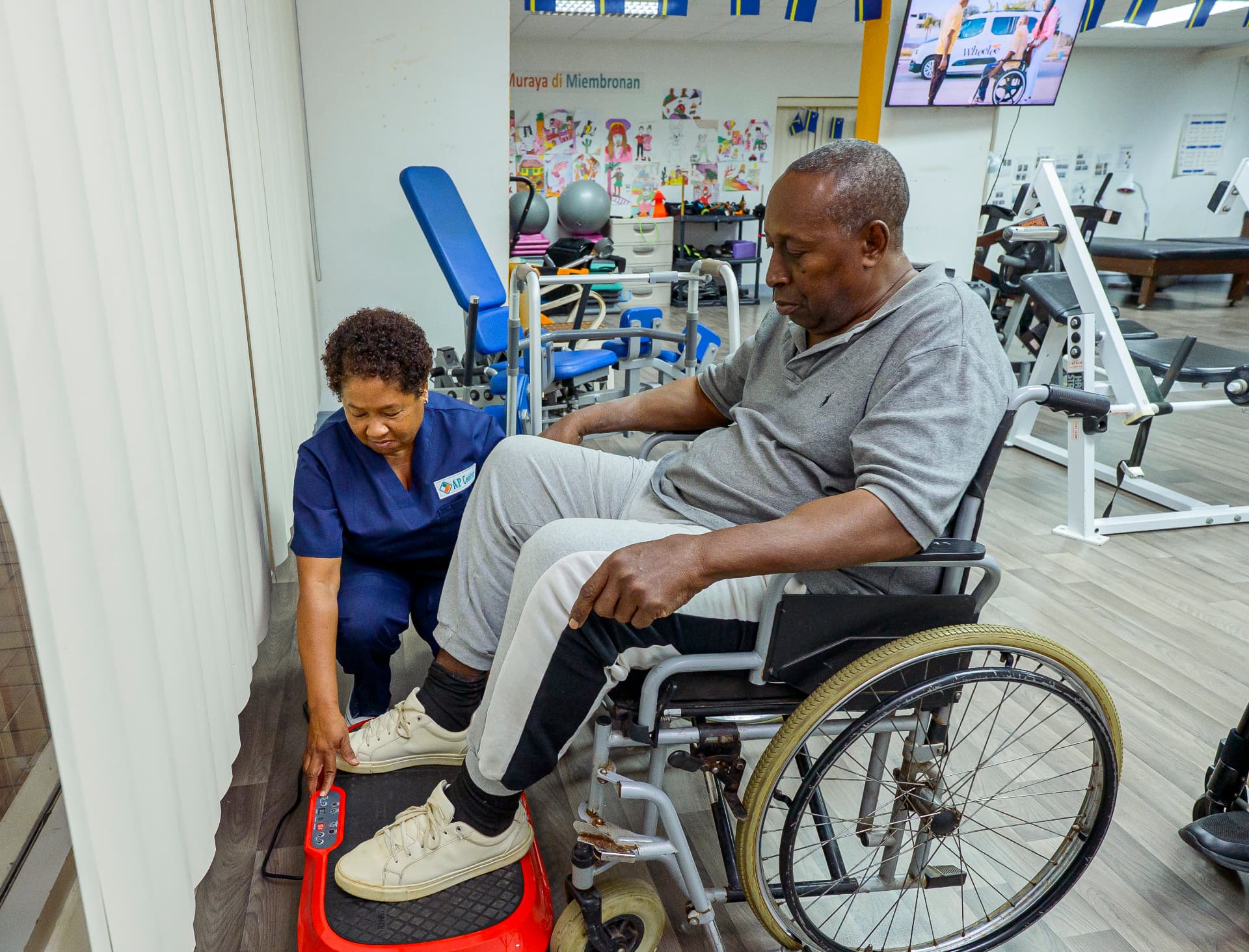 An AP Center floor assistant setting up vibration equipment for a client in a wheelchair.
